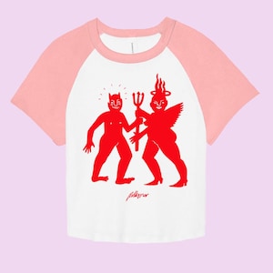 May include: A white and pink baseball tee shirt with a red graphic of a devil and an angel holding a trident. The text "Pelletier" is printed below the graphic.