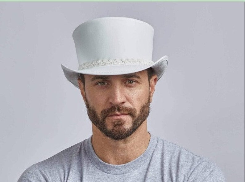 Puede incluir: Un sombrero de copa blanco con una banda trenzada alrededor de la corona. El sombrero est&aacute; hecho de un material liso y parecido al fieltro.