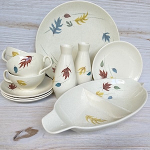 Peut inclure: Un service de vaisselle vintage de couleur crème avec une finition mouchetée et un motif de feuilles. L'ensemble comprend des assiettes, des bols, des tasses, des soucoupes et des vases. Les feuilles sont dans des tons de rouge, jaune et bleu.