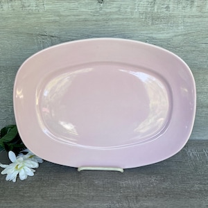 May include: A large, oval-shaped serving platter in a pale pink color. The platter has a slightly raised rim and a smooth, glossy finish.
