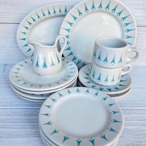 Könnte beinhalten: Ein Vintage-Geschirrset aus weißer Keramik mit türkisfarbenem geometrischem Design. Das Set umfasst Teller, Untertassen, Tassen und einen Sahnekännchen. Die Teller und Tassen sind gestapelt.