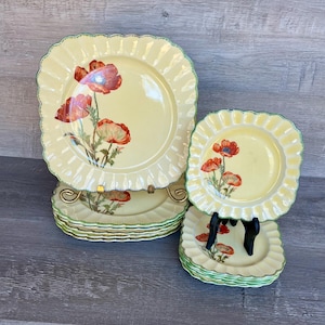 May include: Set of square dinner plates with a yellow background and red poppy flower design. The plates have a scalloped edge and a green trim.