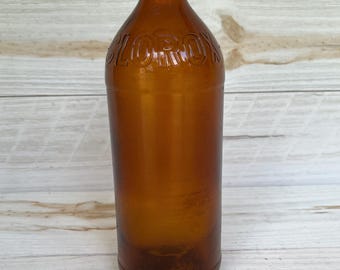 May include: An amber-colored glass bottle with a red and silver cap. The bottle has the embossed word "CLOROX" and is cylindrical in shape. The bottle is empty and appears to be vintage.