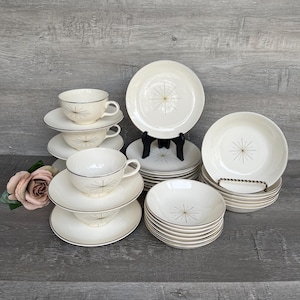 Puede incluir: Un juego de vajilla vintage blanco y dorado con un diseño de estrella. El juego incluye cuencos, platos y tazas de té.