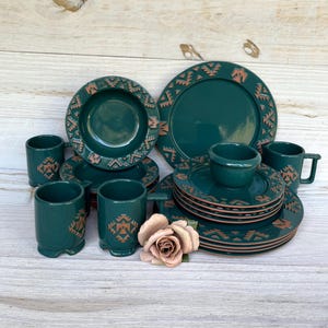 Puede incluir: Un juego de vajilla turquesa completo con un diseño geométrico en un color contrastante. El juego incluye platos, cuencos, tazas y tazas. Una rosa decorativa se coloca cerca de la vajilla.