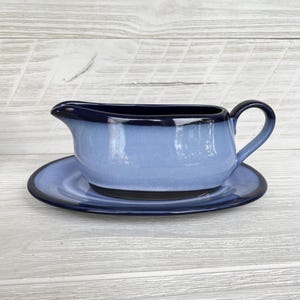 May include: A blue ceramic gravy boat with a matching saucer. The gravy boat has a handle and a spout for easy pouring. The rim and handle are a darker shade of blue, creating a two-tone effect. The set is designed for serving sauces and gravies.