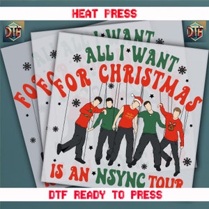 May include: Heat press transfer featuring the text "All I Want For Christmas Is An *NSYNC Tour" in red and green. The design includes a cartoon illustration of five people and snowflakes. The words "HEAT PRESS" and "DTF READY TO PRESS" are also visible.