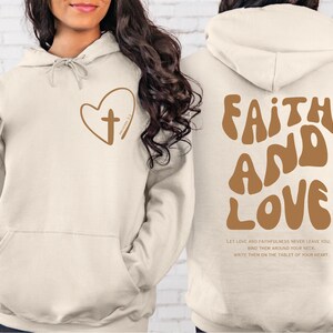 a woman wearing a white hoodie with the words faith and love printed on it