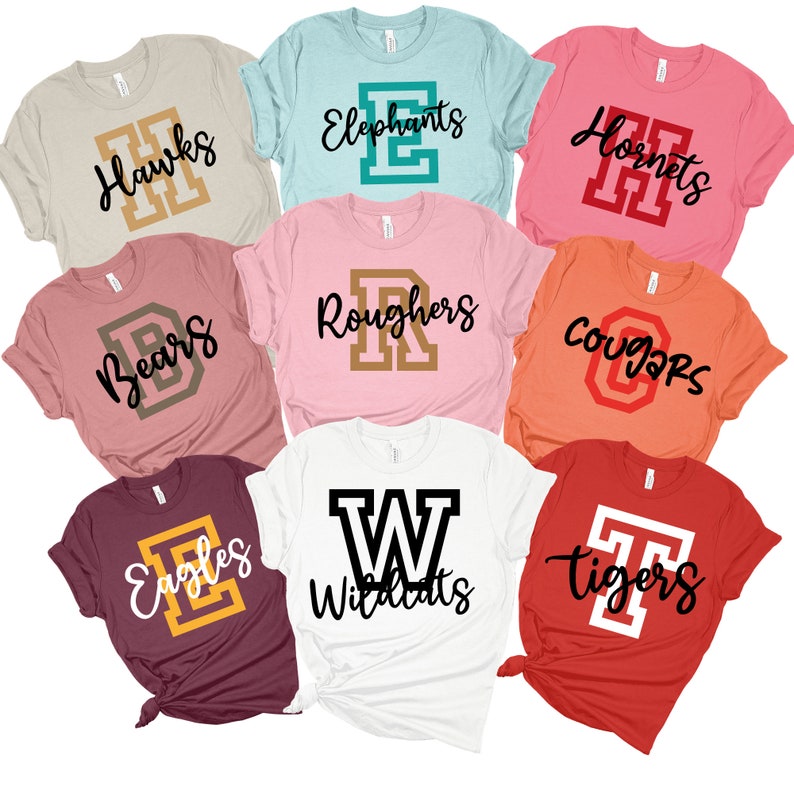 May include: Nine different t-shirts with various school team names and logos. The shirts are in different colours, including pink, red, white, orange, beige, and maroon. The logos are in different colours, including gold, black, red, and teal.