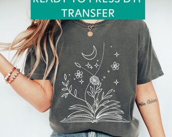 May include: A grey t-shirt with a white design of a book with flowers and a crescent moon. The text "Mon Océan" is visible on the right sleeve.
