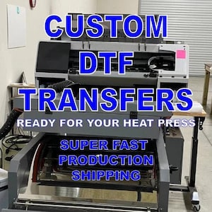 May include: A close-up of a large, industrial-style printer with the text "CUSTOM DTF TRANSFERS" in blue letters. The text "READY FOR YOUR HEAT PRESS" is below the main text. The printer is on a stand with a metal platform. The text "SUPER FAST PRODUCTION SHIPPING" is on the platform.
