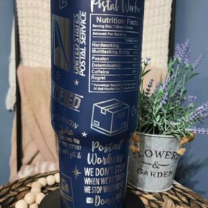 May include: A blue stainless steel tumbler with a silver design. The tumbler features a graphic of a mail truck, a mailbox, and a heart. The text "Postal Worker" and "We don't stop when we're tired, we stop when we're done" is printed on the tumbler.