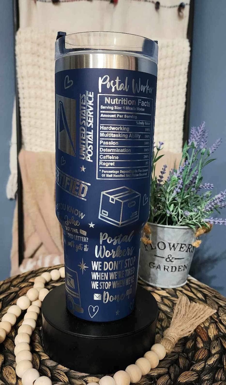 May include: A blue stainless steel tumbler with a silver design. The tumbler features a graphic of a mail truck, a mailbox, and a heart. The text "Postal Worker" and "We don't stop when we're tired, we stop when we're done" is printed on the tumbler.