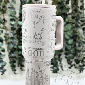 May include: A pink stainless steel tumbler with a white design featuring bible verses, floral elements, and the words "Be the light", "No worries, God got me", and "Strong in the Lord". The tumbler has a handle and a straw.