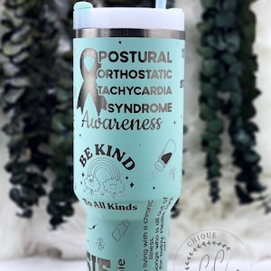 Puede incluir: Un vaso de acero inoxidable con un diseño azul claro y blanco. El vaso presenta una cinta turquesa, las palabras "Postural Orthostatic Tachycardia Syndrome Awareness" y la frase "Be Kind to All Kinds".