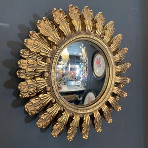 Peut inclure: Un miroir soleil doré avec un miroir rond convexe au centre. Le miroir est entouré d'un cadre décoratif avec un motif soleil.