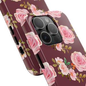Könnte beinhalten: Burgunderfarbene Handyhülle mit einem floralen Muster aus rosa Rosen und grünen Blättern. Die Hülle hat eine glänzende Oberfläche und einen Kameraausschnitt. Das Blumenmuster wiederholt sich auf der Oberfläche.