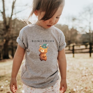 May include: A gray t-shirt with a cartoon bear wearing a green hat and the text "Kleines Barchen" printed on the front.