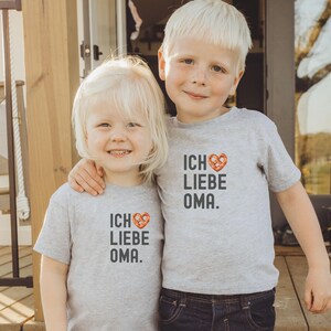 May include: Two children wearing grey t-shirts with the text "Ich Liebe Oma" and a pretzel heart graphic. The child on the left is a girl and the child on the right is a boy.