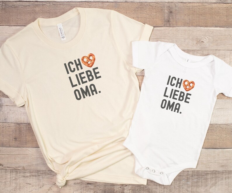 May include: Two white t-shirts with the text "Ich liebe Oma" and a pretzel heart graphic. The larger shirt is a long-sleeved t-shirt and the smaller shirt is a short-sleeved bodysuit.