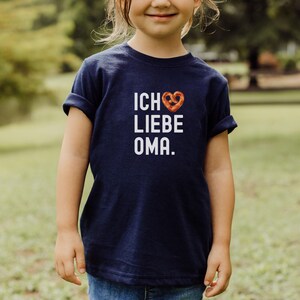 May include: A navy blue t-shirt with white text that reads "Ich liebe Oma" with a pretzel-shaped heart.