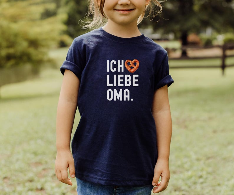 May include: A navy blue t-shirt with white text that reads "Ich liebe Oma" with a pretzel-shaped heart.