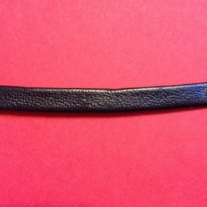 Könnte beinhalten: Nahaufnahme eines schwarzen Lederriemens. Der Riemen ist glatt und hat eine subtile Textur.