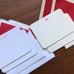 May include: Two stacks of white note cards with red trim and red lettering. The top stack has the initials "SHJ" and the bottom stack has the name "Liz Cayfield".