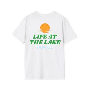 May include: A white short-sleeve t-shirt featuring a graphic on the back. The design includes an orange sun above the green text LIFE AT THE LAKE and the light blue text SALTY GULL. The shirt has a crew neckline and a standard fit.