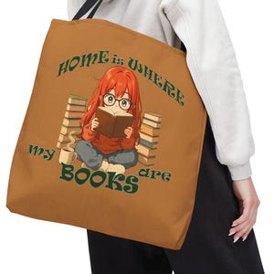 May include: A tan tote bag featuring an anime-style illustration of a girl reading a book, surrounded by stacks of books and a coffee mug. The text "HOME is WHERE my BOOKS are" is printed in green.