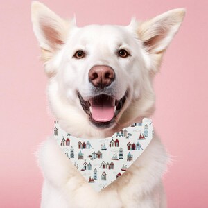 May include: A white dog wearing a patterned bandana featuring red, blue, and grey beach huts, boats, and lighthouses. The dog is smiling with its tongue visible, set against a pink backdrop.