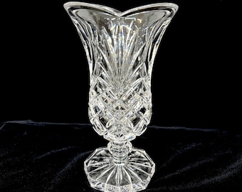 May include: A clear, cut-glass vase with a flared top and a diamond pattern. The vase sits on a pedestal base with a geometric design. The vase is approximately 10 inches tall.