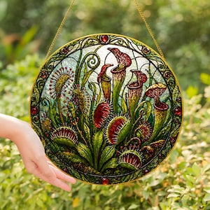 May include: A round stained glass window featuring a botanical design of carnivorous plants. The artwork includes pitcher plants, Venus flytraps, and sundews in shades of red, green, and yellow, with a gold-colored border and hanging chain.