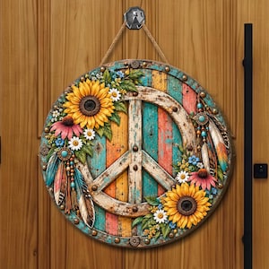 May include: A round wooden wall sign featuring a central peace symbol over a multicolored vertical plank background. The design is decorated with large yellow sunflowers, pink and white flowers, green leaves, and hanging feather ornaments.