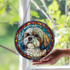May include: Round stained glass window featuring a Shih Tzu dog portrait. The artwork has a colorful, mosaic-like design with a blue, red, and yellow border. The dog's name, "Rocky," is written at the bottom.