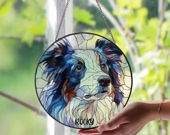 May include: Round stained glass window art featuring a dog's portrait. The dog has blue, white, and brown fur, with the name "Rocky" in a black font. The artwork is framed in black and hangs from a chain.