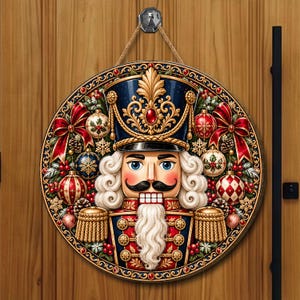 May include: A circular wall hanging featuring a detailed nutcracker illustration in a dark blue and red uniform with gold accents. The nutcracker is surrounded by a festive wreath of red bows, patterned Christmas ornaments, and pine cones.