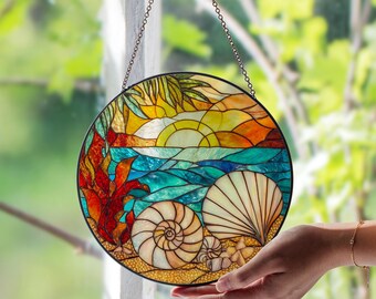 Puede incluir: Una vidriera redonda que representa una escena de playa con una puesta de sol, el océano y conchas marinas. La obra de arte presenta colores vibrantes como el amarillo, naranja, azul y blanco. La ventana está colgada de una cadena.