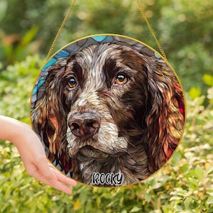 May include: Round stained glass window art featuring a detailed portrait of a brown and white dog. The dog's name, "Rocky", is printed in white at the bottom. The artwork is framed in gold and hangs from a gold chain.