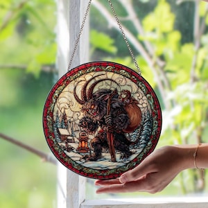 Può includere: Vetrata rotonda raffigurante Krampus, una figura cornuta, che trasporta un sacco e un bastone, con una bambina sulla schiena. L'opera d'arte è ambientata in un paesaggio invernale innevato con un bordo rosso e verde, appesa a una catena.