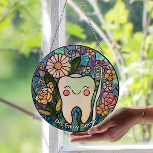 Peut inclure: Vitrail rond représentant une dent souriante, une brosse à dents et des motifs floraux. Le design présente une dent joyeuse avec des joues roses, entourée de fleurs roses, jaunes et bleues. Le texte "Dr. Emily Smith" est en bas.