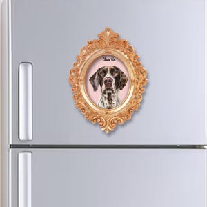 May include: A gold-coloured framed magnet with a portrait of a German Shorthaired Pointer dog named Charlie. The dog has brown and white markings, set against a pink background. The frame is ornate.
