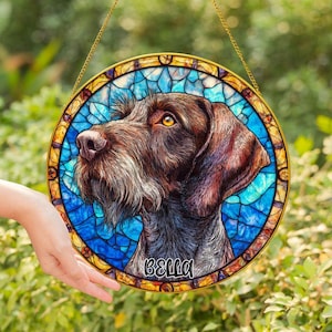 Puede incluir: Arte de ventana de vidriera redonda con un retrato de perro. El perro tiene pelaje marrón, barba blanca y ojos amarillos. El fondo es azul con efecto vidriera. El nombre "BELLA" está escrito en la parte inferior.