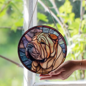 May include: Round stained glass window featuring a Shar Pei dog. The artwork uses shades of brown, orange, and blue. The dog's face is the focal point, with detailed wrinkles and a gentle expression. A metal chain is attached for hanging.