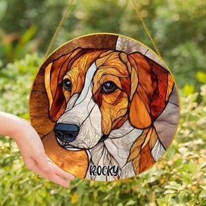 May include: Round stained glass window art featuring a dog's face with brown, white, and orange hues. The dog's name, "Rocky," is written in black script. The artwork is framed in gold and hangs from a gold chain.