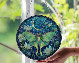 May include: Round stained glass window art featuring a green moth with detailed wings, a crescent moon, and floral accents. The artwork is predominantly blue and green, with a chain for hanging. The design is reminiscent of a mosaic.