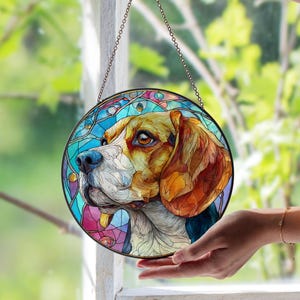 Könnte beinhalten: Ein rundes Buntglasfenster mit einem Beagle-Hund. Der Hund hat braunes und hellbraunes Fell, eine blaue Nase und braune Augen. Der Hintergrund ist ein Mosaik aus blauem, rosa und violettem Glas. Das Fenster ist schwarz umrandet und hängt an einer Kette.