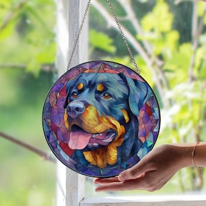 Könnte beinhalten: Runde Glasmalerei mit einem Rottweiler-Hund. Der Hund hat schwarzes, braunes und beiges Fell mit einer rosa Zunge. Der Hintergrund ist ein Mosaik aus lila, blauen und roten Glasteilen. Das Kunstwerk hängt an einer Kette.