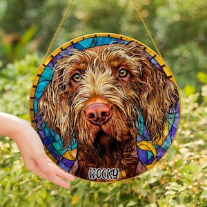 May include: Round stained glass window featuring a detailed portrait of a brown dog with the name "Rocky" at the bottom. The dog's fur is a mix of brown and tan, with a pink nose and expressive eyes. The border is a mosaic of blue, purple, and yellow.