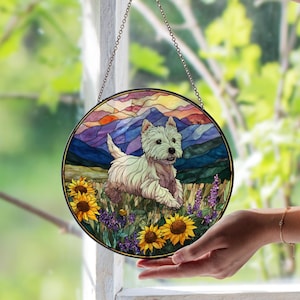 May include: Round stained glass window art featuring a West Highland White Terrier dog in a field of sunflowers and lavender. The background depicts mountains and a sunset. The artwork is suspended by a chain.